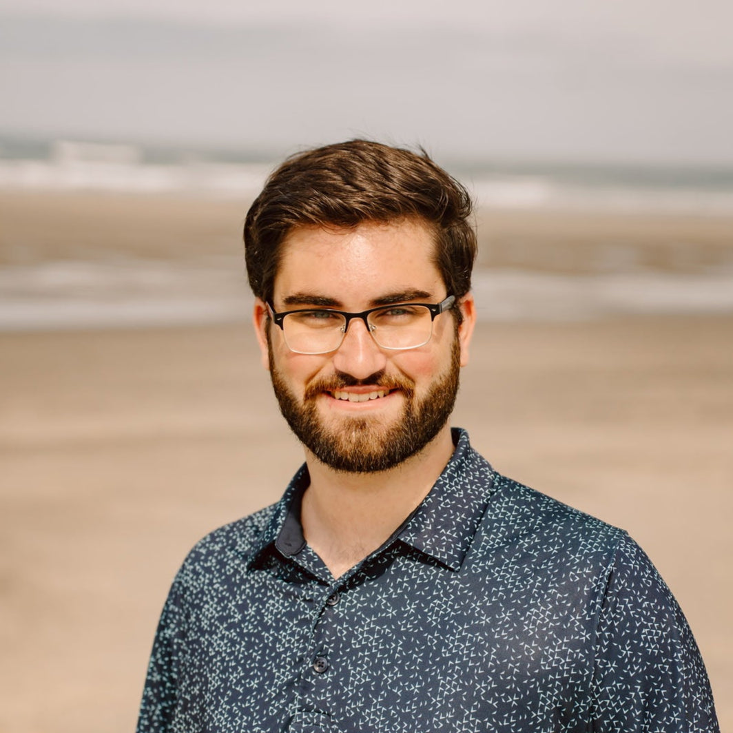 Man with glasses and a beard standing on a beach