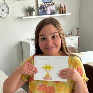 Young girl holding up a drawing of a cartoon giraffe character dinkers the giraffe for dinkers glazed nuts